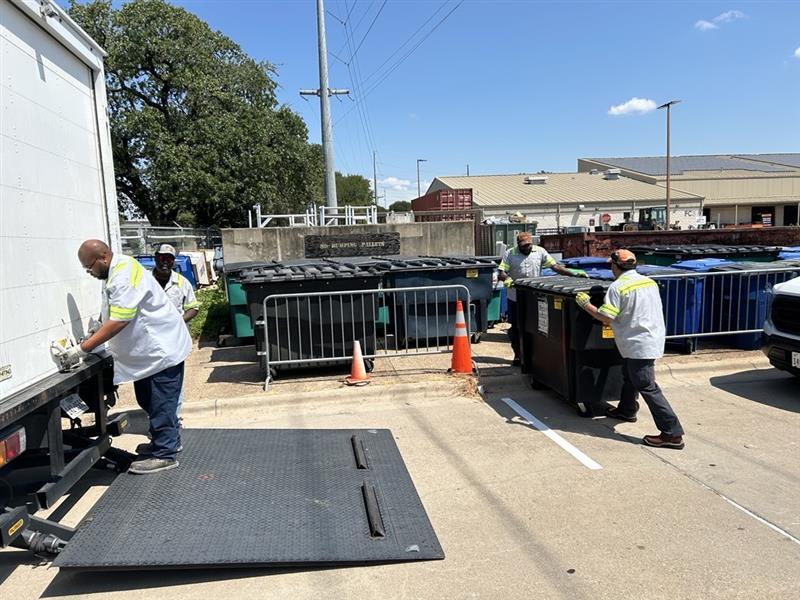Milton Roberson Jr., SWR team lead, secures the door on a box truck used to retrieve 1.5-yard dumpsters from a special campus event. Tim Williams, an SWR worker, operates the lift gate while SWR workers Lawrence Clark and Richard Hernandez return dumpsters to the storage yard for future use. An empty 1.5-yard dumpster weighs 300 pounds.